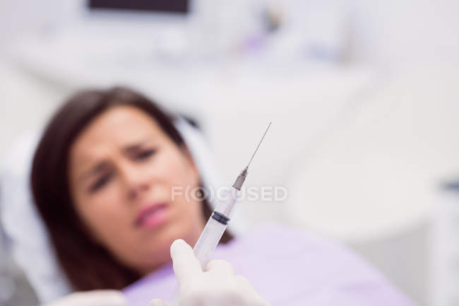 Dentist holding syringe in front of scared patient in clinic — Stock Photo