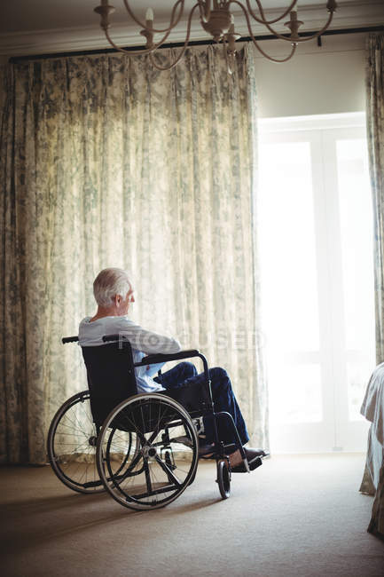 Hombre mayor sentado en silla de ruedas en el dormitorio en casa - foto de stock