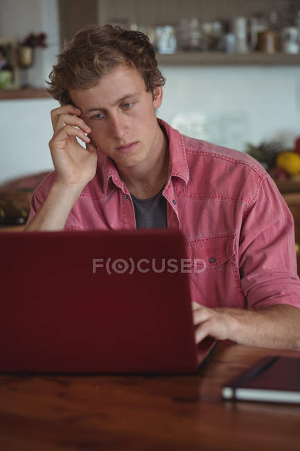 Hombre preocupado usando el ordenador portátil en la cocina - foto de stock