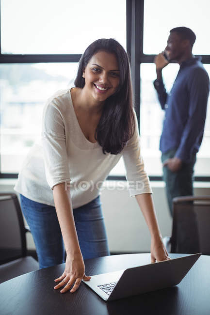 Retrato de mulher de negócios inclinada na mesa e sorrindo para a câmera no escritório — Fotografia de Stock