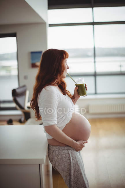 Femme enceinte réfléchie buvant du jus à la maison — Photo de stock