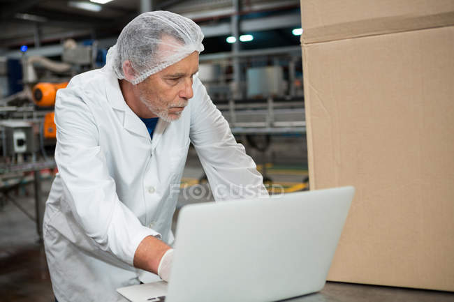 Серйозний працівник чоловічої статі використовує ноутбук на заводі холодного напою — стокове фото