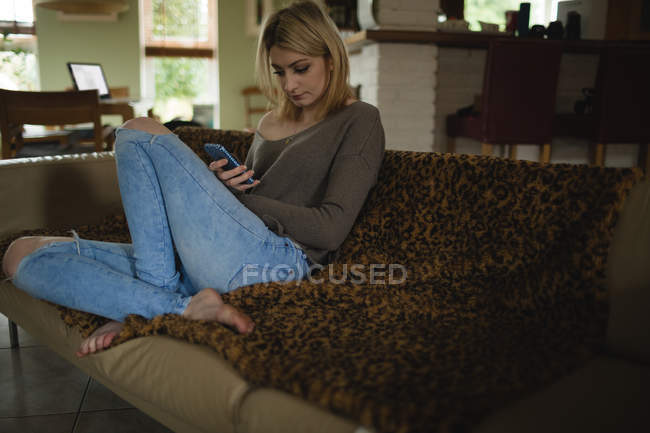 Frau liegt und benutzt Handy auf Couch im Wohnzimmer — Stockfoto