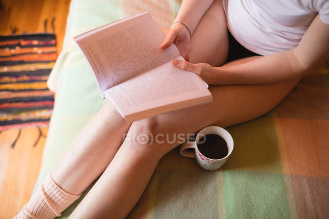 Femme assise sur le lit et lisant un livre à la maison — Photo de stock