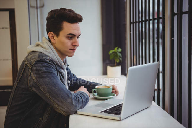 Mann schaut auf Laptop, während er Kaffee im Café hält — Stockfoto
