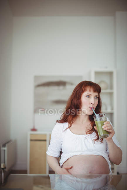 Thoughtful pregnant woman drinking juice at home — Stock Photo
