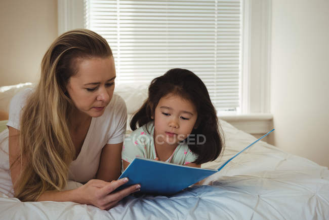 Mother and daughter reading a book in bedroom at home — Stock Photo
