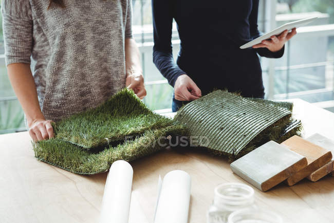 Business executives examining artificial turf while using digital tablet in office — Stock Photo