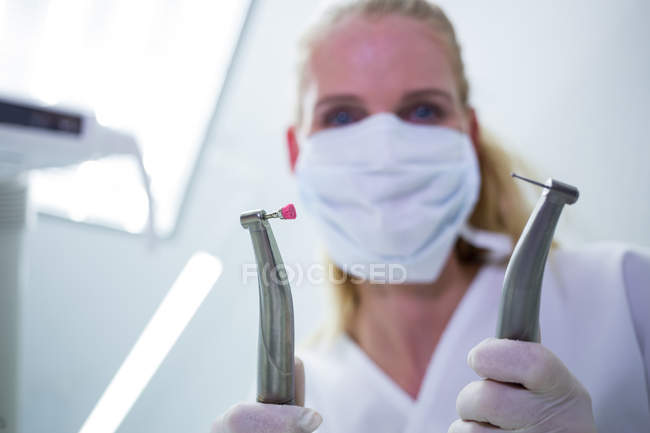 Dentista feminina com máscara cirúrgica segurando instrumentos dentários na clínica — Fotografia de Stock