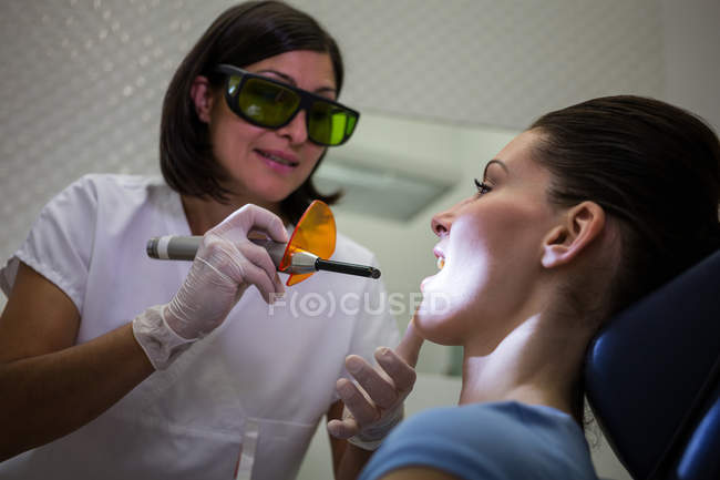 Dentista examinando dentes jovens de pacientes com luz de cura dentária na clínica — Fotografia de Stock