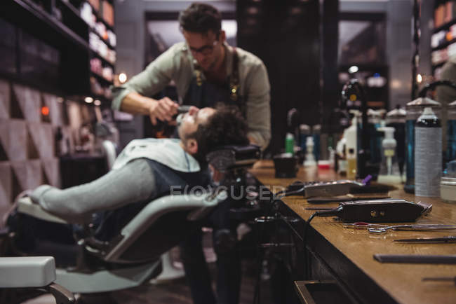Различные триммеры на туалетном столике с парикмахерской бритья клиента на заднем плане в парикмахерской — стоковое фото