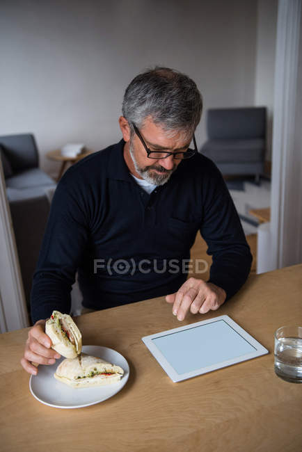 Человек, использующий цифровой планшет во время завтрака дома — стоковое фото