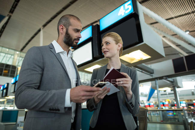 Personnes d'affaires titulaires d'une carte d'embarquement et utilisant un téléphone portable dans un terminal d'aéroport — Photo de stock