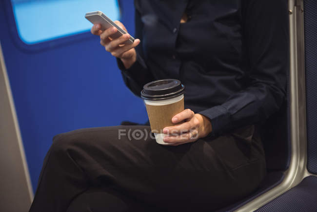 Meados de seção de empresária com xícara de café usando telefone enquanto sentado no trem — Fotografia de Stock