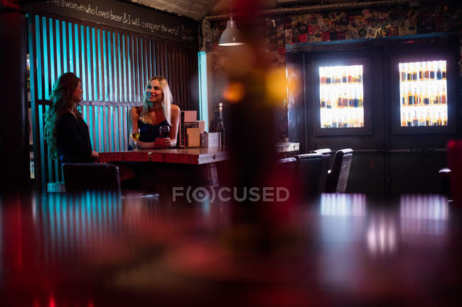 Hermosas mujeres interactuando mientras toman vino en el bar - foto de stock