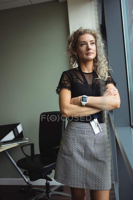 Pensativa mujer de negocios de pie con los brazos cruzados en la oficina - foto de stock