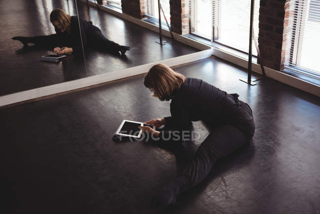 Danseuse s'étirant sur le sol et utilisant un téléphone portable dans un studio de danse — Photo de stock