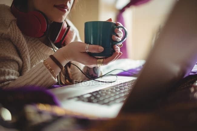 Mulher bonita usando laptop enquanto toma café na cama em casa — Fotografia de Stock