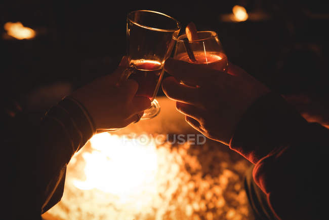 Coupé les mains du couple tenant des boissons contre la cheminée brûlante la nuit pendant l'hiver — Photo de stock