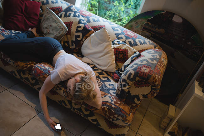 Mulher deitada e usando telefone celular no sofá na sala de estar em casa — Fotografia de Stock