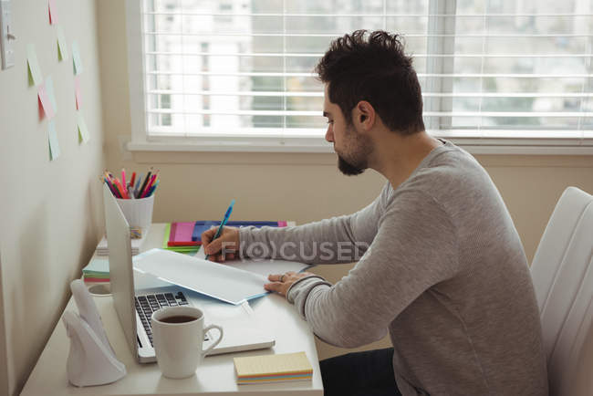 Homem atento escrevendo no documento enquanto sentado na mesa — Fotografia de Stock