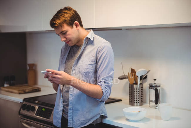 Hombre usando el teléfono móvil mientras se prepara el desayuno en la cocina en casa - foto de stock