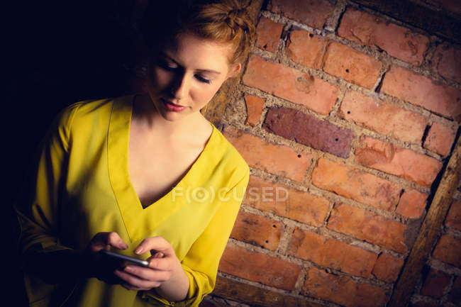 Mulher de pé contra a parede de tijolo e usando telefone celular — Fotografia de Stock