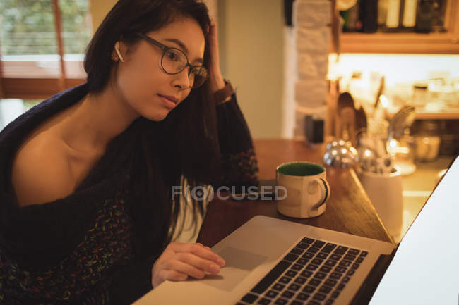 Mujer usando el ordenador portátil en el mostrador de cocina en casa - foto de stock