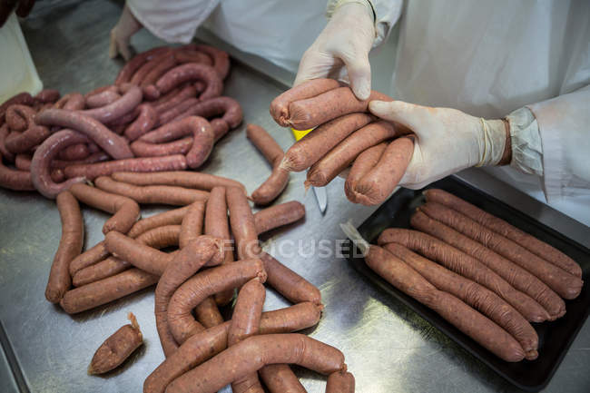 Mani di macellai che imballano salsicce crude in fabbrica di carne — Foto stock