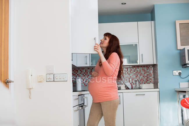 Mulher grávida à procura de comida no armário na cozinha em casa — Fotografia de Stock