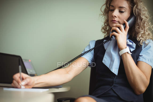 Empresaria hablando por teléfono y escribiendo en bloc de notas en la oficina - foto de stock