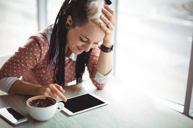 Woman using digital tablet while having cup of coffee in cafe — Stock Photo