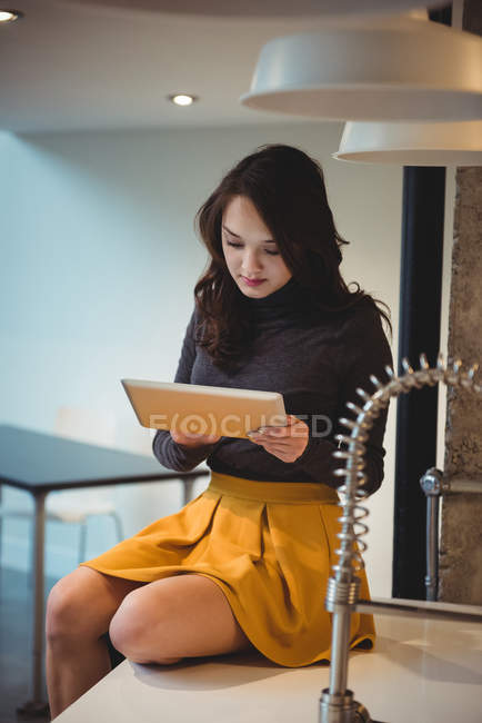 Donna seduta sul piano di lavoro della cucina con tablet digitale a casa — Foto stock