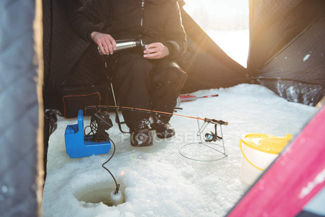 Mid section of ice fisherman pouring coffee in tent — Stock Photo