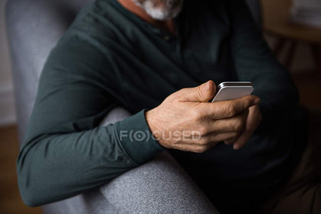 Средняя часть человека с помощью мобильного телефона в гостиной на дому — стоковое фото