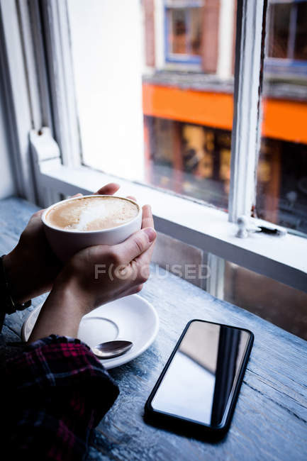 Primer plano de la mano de la mujer sosteniendo la taza de café en la cafetería - foto de stock