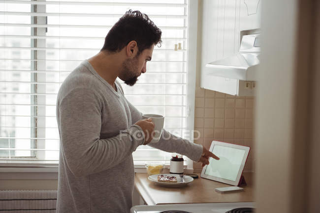 Людина використовує цифровий планшет, маючи каву на кухні — стокове фото