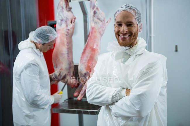 Retrato del carnicero de pie con los brazos cruzados en la fábrica de carne - foto de stock