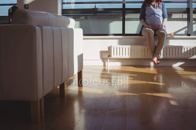Donna incinta seduta vicino alla finestra in soggiorno a casa — Foto stock