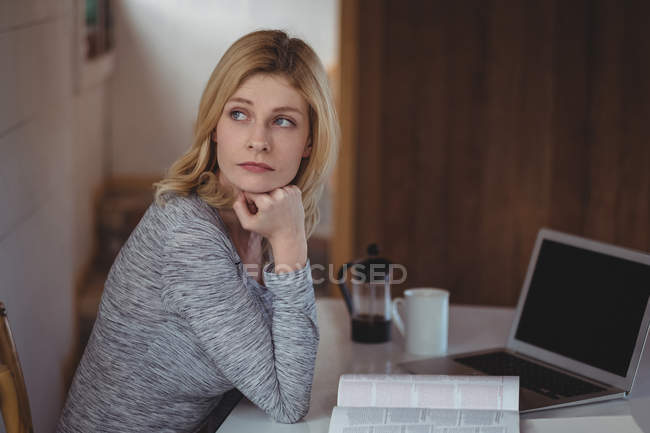 Продумана жінка сидить за столом вдома — стокове фото