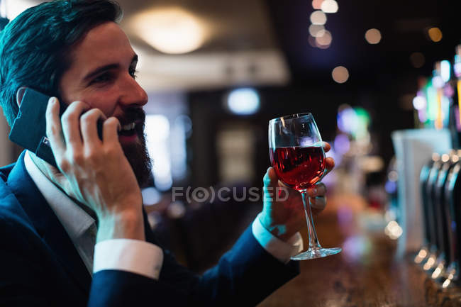 Homme d'affaires parlant sur téléphone portable tout en prenant un verre de vin dans le bar — Photo de stock