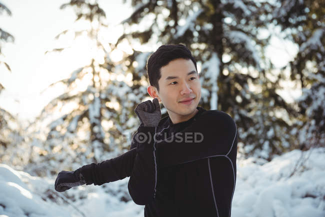 Hombre sonriente estirando los brazos en el bosque durante el invierno - foto de stock