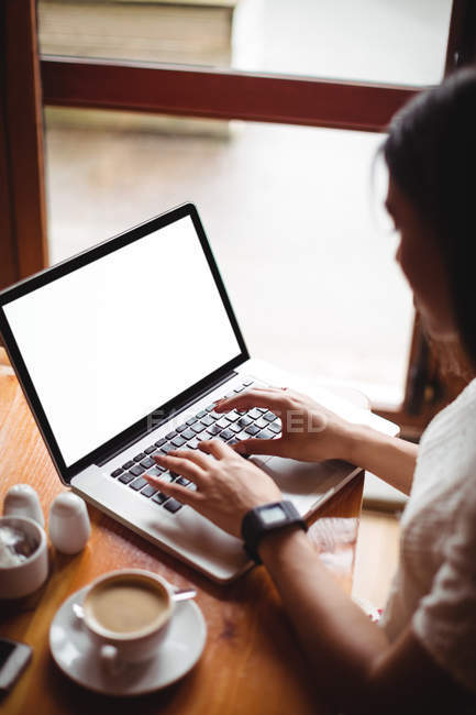 Жінка дивиться час під час використання ноутбука в кафе — стокове фото