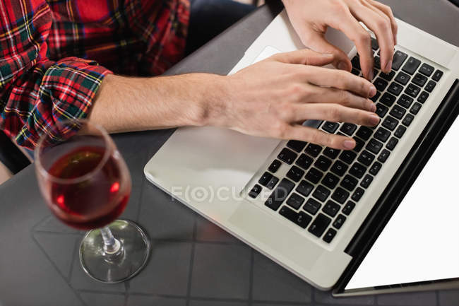 Mains de l'homme en utilisant un ordinateur portable avec verre à vin sur la table dans le bar — Photo de stock