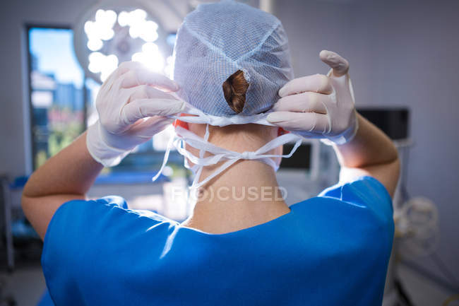 Vista trasera de la enfermera con gorra quirúrgica en quirófano en el hospital - foto de stock