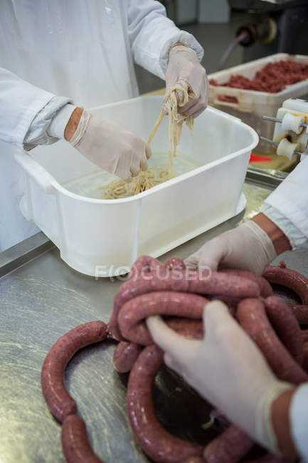 Mid-section of butchers processing sausages in meat factory — Stock Photo
