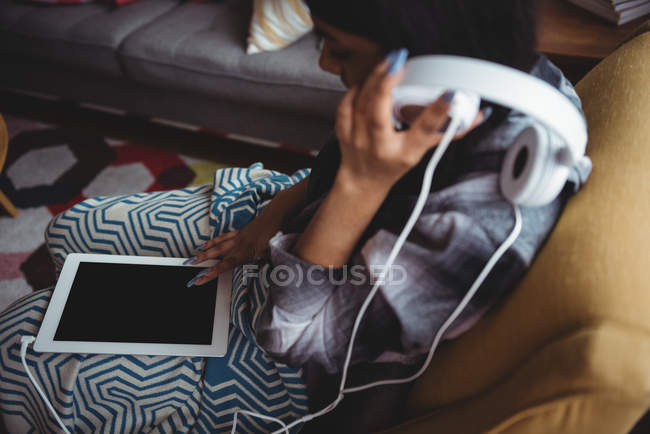 Donna che ascolta musica con cuffie e tablet digitale in salotto a casa — Foto stock