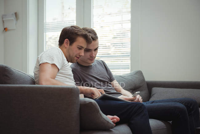 Pareja gay usando tableta digital en sala de estar en casa - foto de stock