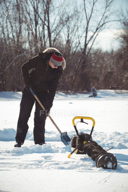 Pêcheur sur glace creusant de la neige avec une pelle dans un paysage enneigé — Photo de stock