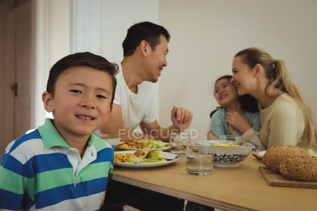 Портрет хлопчика, який посміхається, коли сім'я їсть у фоновому режимі вдома — стокове фото